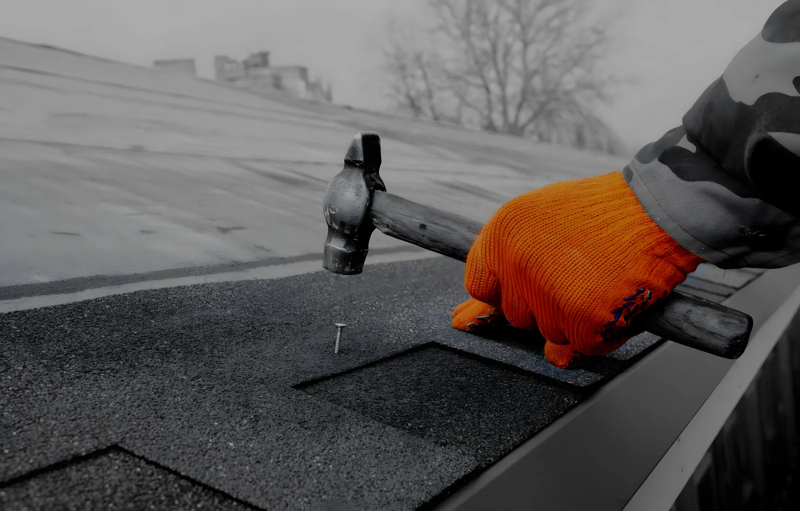 Gant orange, marteau et clou posés sur un bardeau d’asphalte